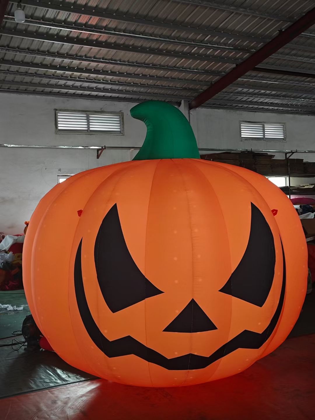 Large orange jack-o-lantern inflatable fully inflated on a factory floor for testing.